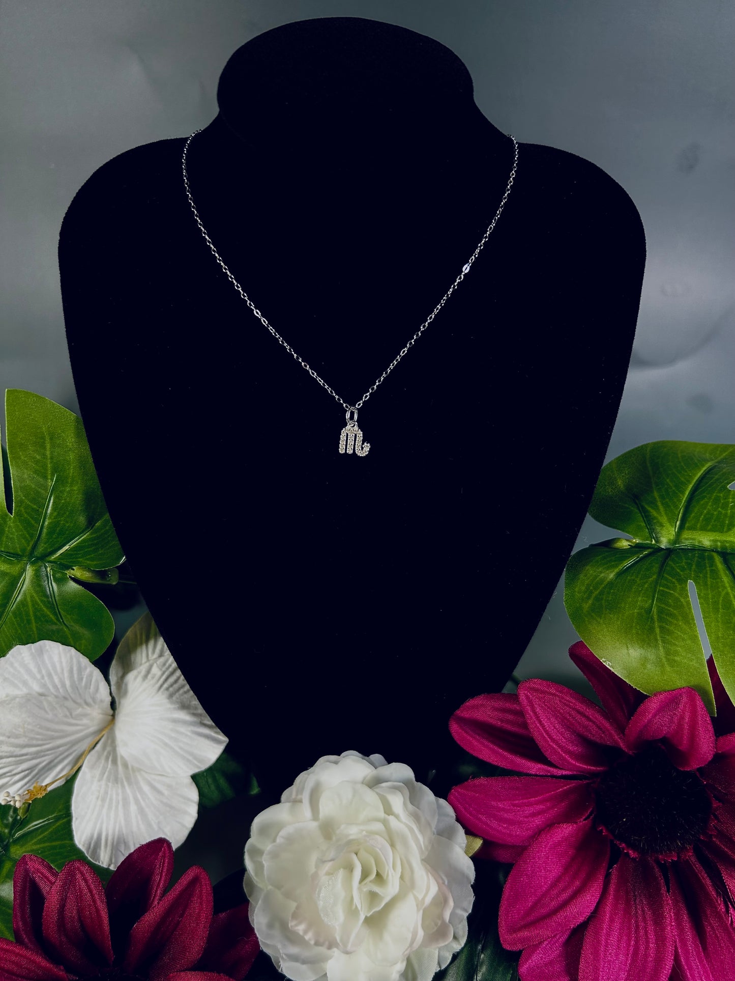 Freya Canada’s Scorpio Goddess Pave Charm Necklace. Pictured with tropical flowers and leaves. Displayed on a black velvet jewelry bust. Ships from Vancouver, B.C.