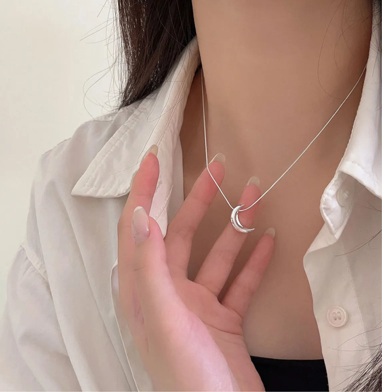 Model is wearing Freya Canada’s I AM SELENE sterling silver luminous crescent moon necklace. Close up of neck with her hand holding crescent moon charm.