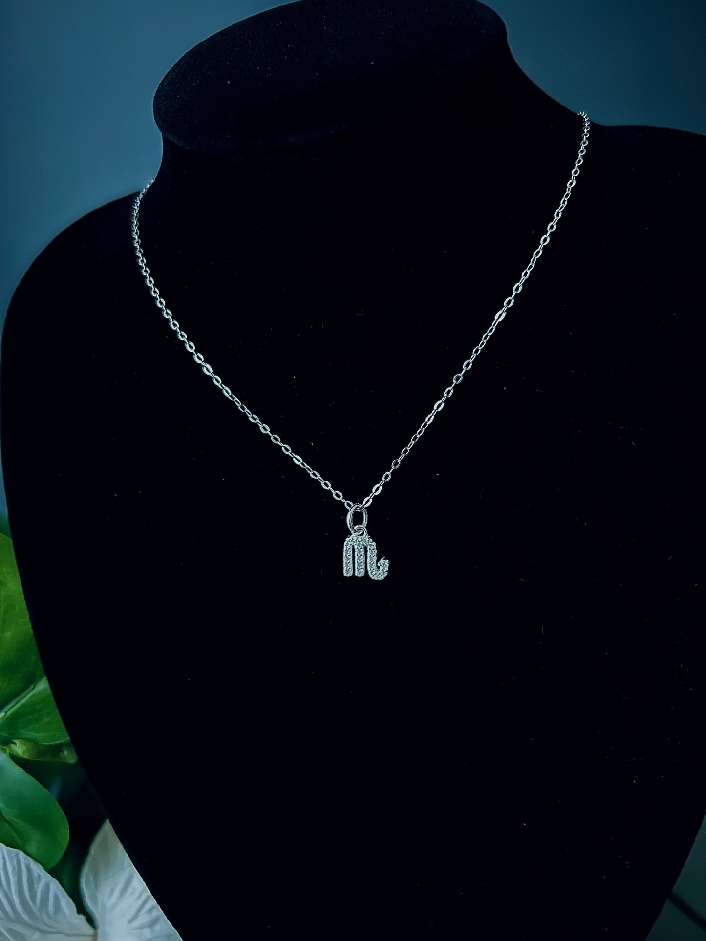Freya Canada’s Scorpio Goddess Pave Charm Necklace. Pictured with tropical flowers and leaves. Displayed on a black velvet jewelry bust. Ships from Vancouver, B.C.