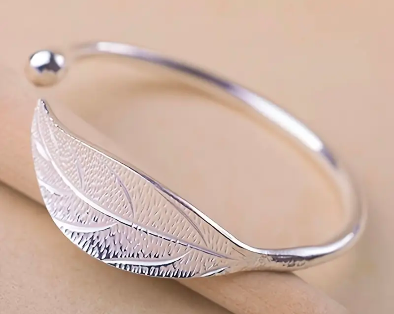 Pictured on a peachy beige table, the I AM ARTEMIS Wild One Leaf Bangle from Freya Canada. Ships from Vancouver BC.