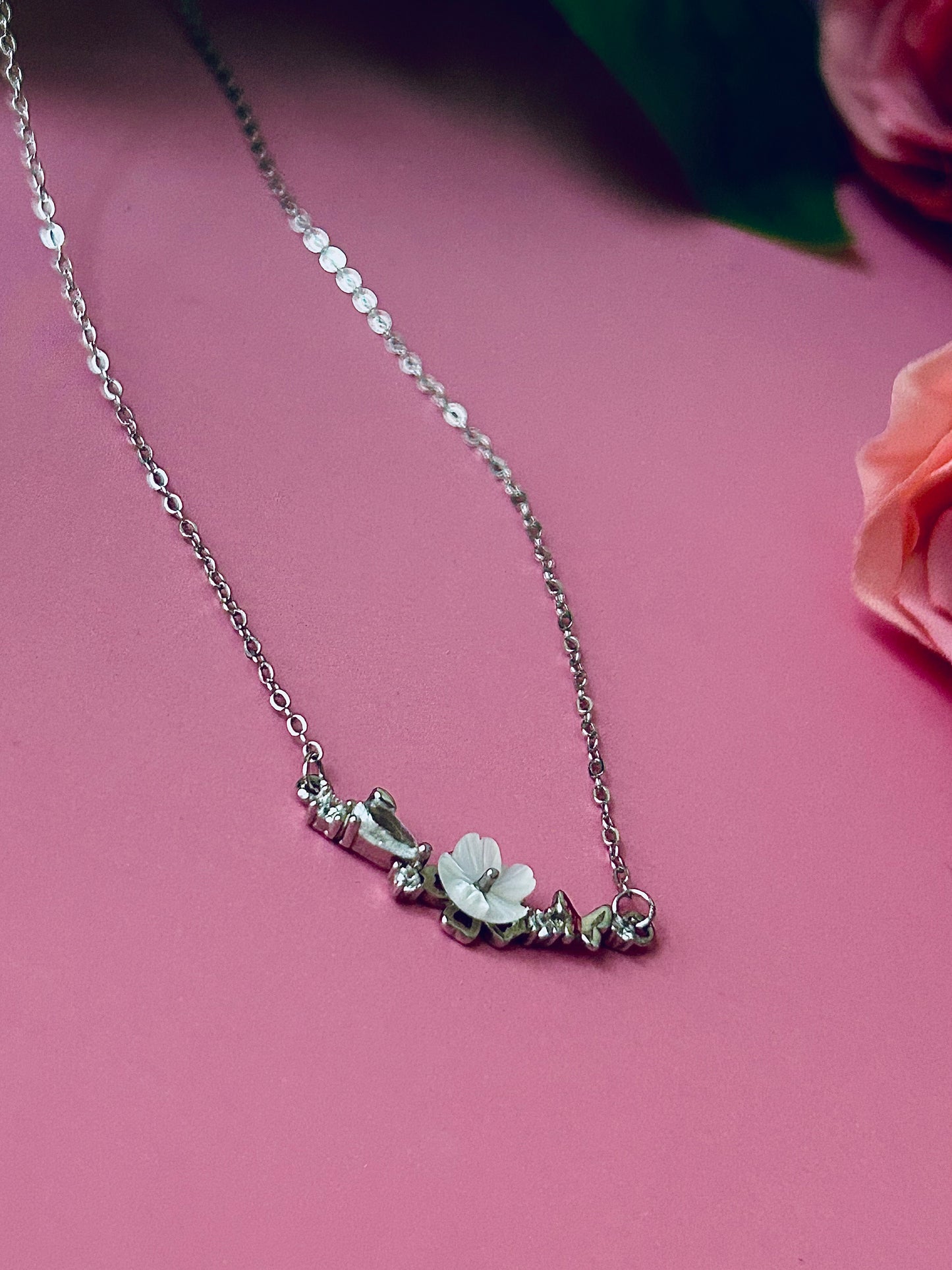 Freya Canada’s I AM FLORA Glass Petals Necklace pictured on a bubblegum pink background with roses. The necklace features a solid silver butterfly, zircon crystal dew drops and a mother of pearl hand carved flower centre