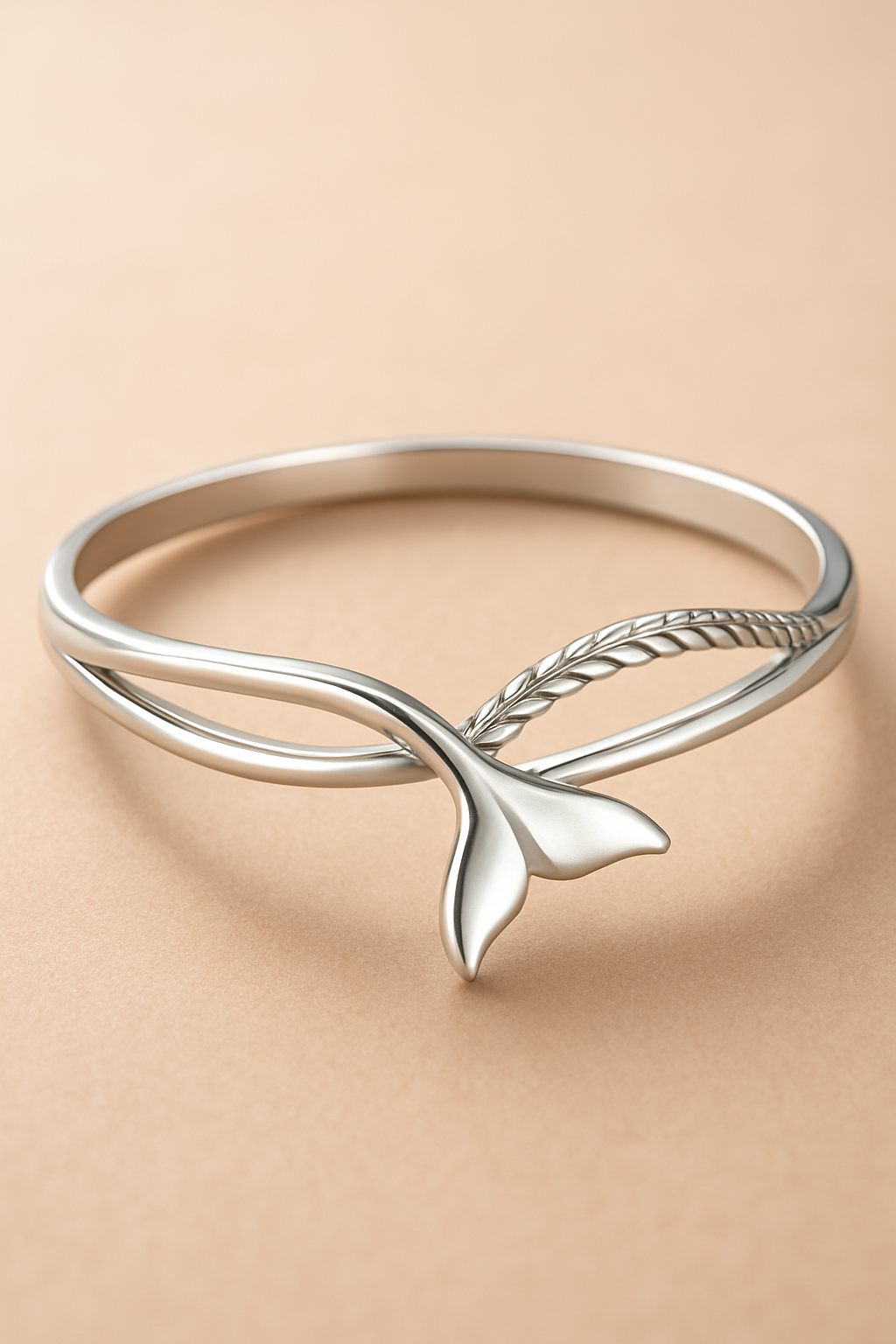 A ring in sterling silver with a fish tail design, water wave and carved rope design on a peachy beige background