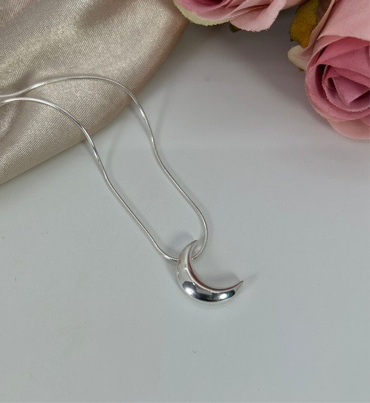 Freya Canada’s I AM SELENE sterling silver luminous crescent moon necklace. Close up, flat lay with pink roses and cream coloured silk fabric elements. 