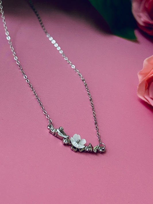 Freya Canada’s I AM FLORA Glass Petals Necklace pictured on a bubblegum pink background with roses. The necklace features a solid silver butterfly, zircon crystal dew drops and a mother of pearl hand carved flower centre 