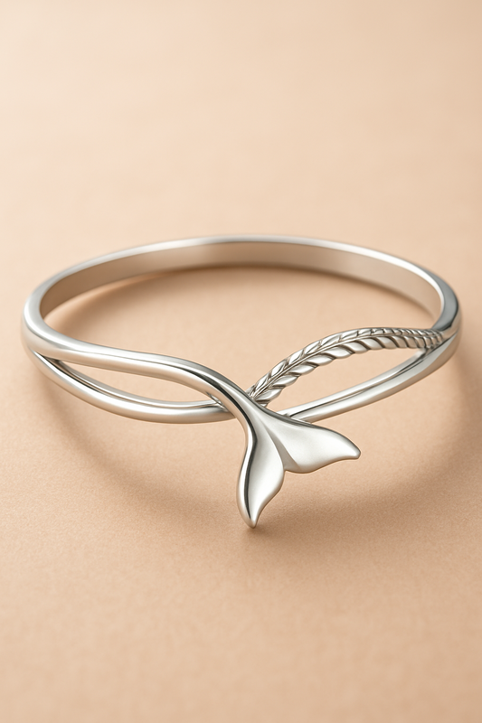 A ring in sterling silver with a fish tail design, water wave and carved rope design on a peachy beige background 